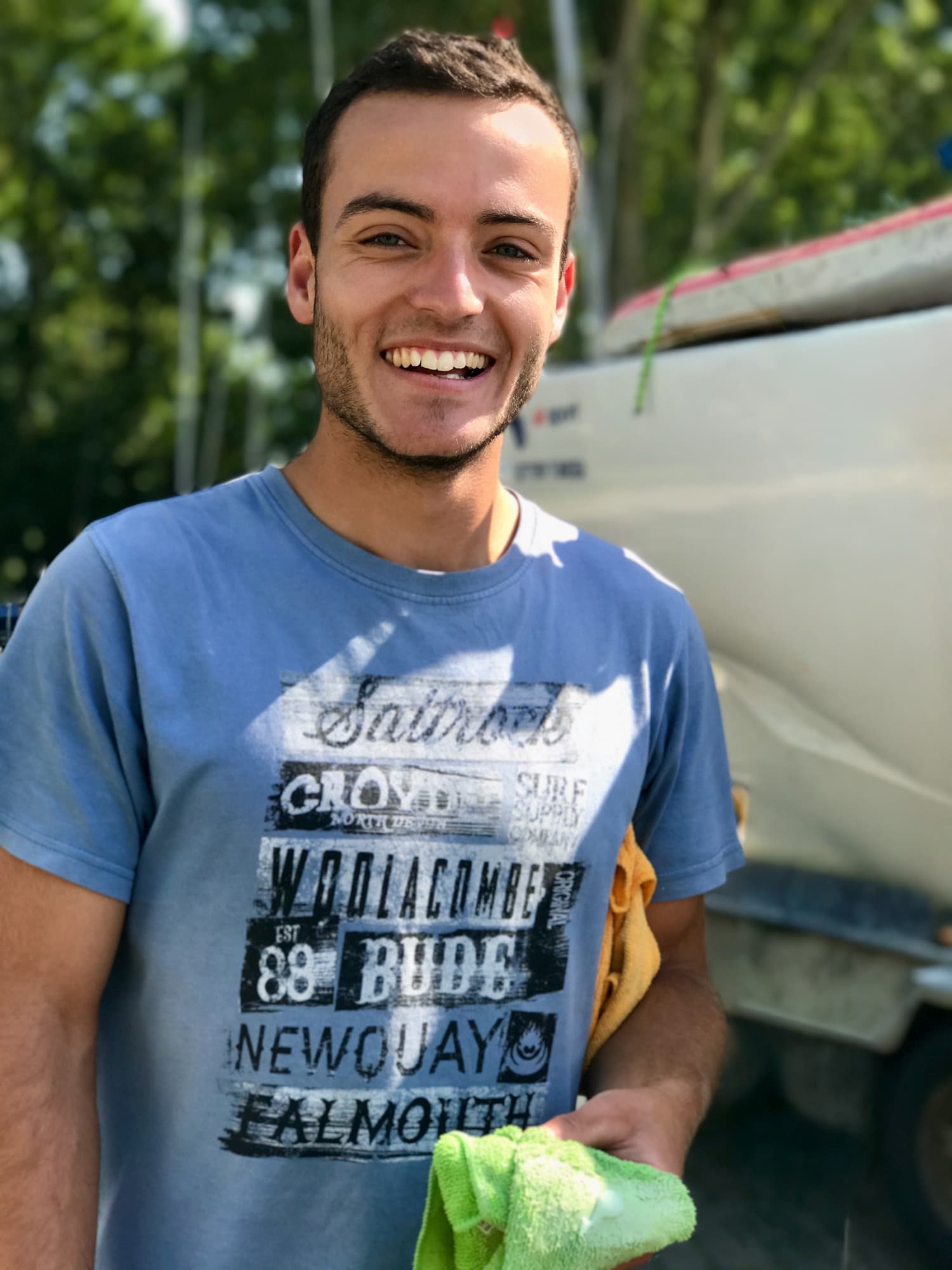 A smiling young sailor in a blue shirt beside his 2.4mR