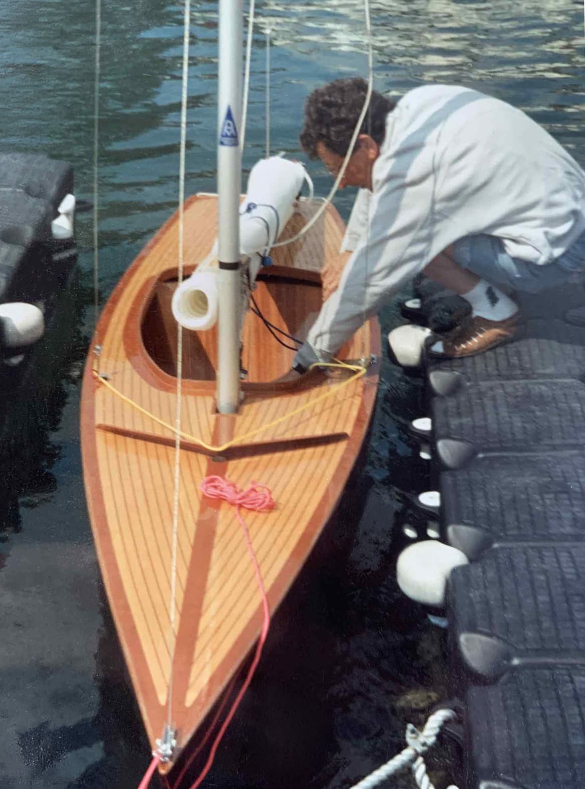 A varnished wooden Norlin 2.4mR being rigged alongside a dock.