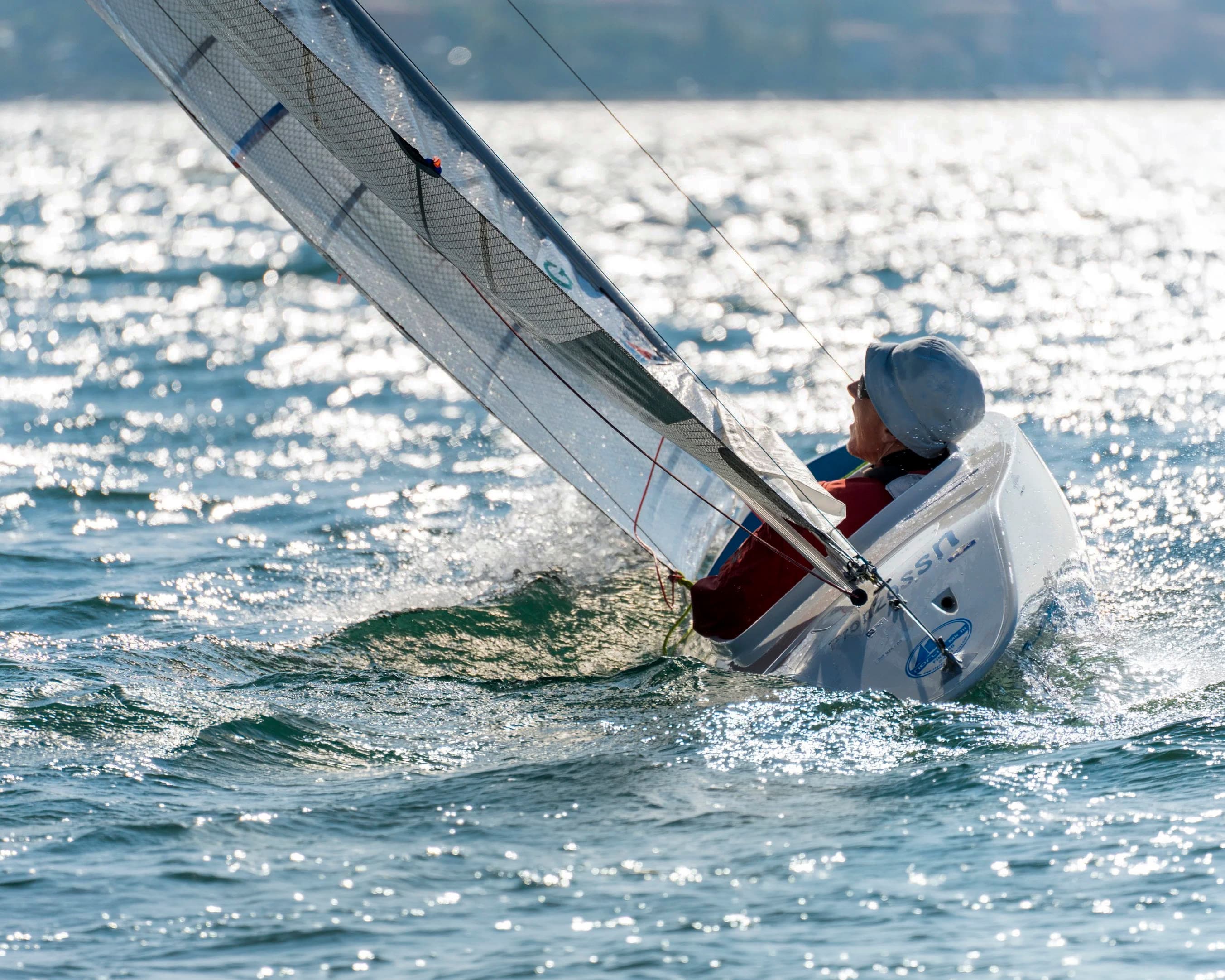 A 2.4mR sailing across glittering water, the sailor low in the cockpit under a backlit rig