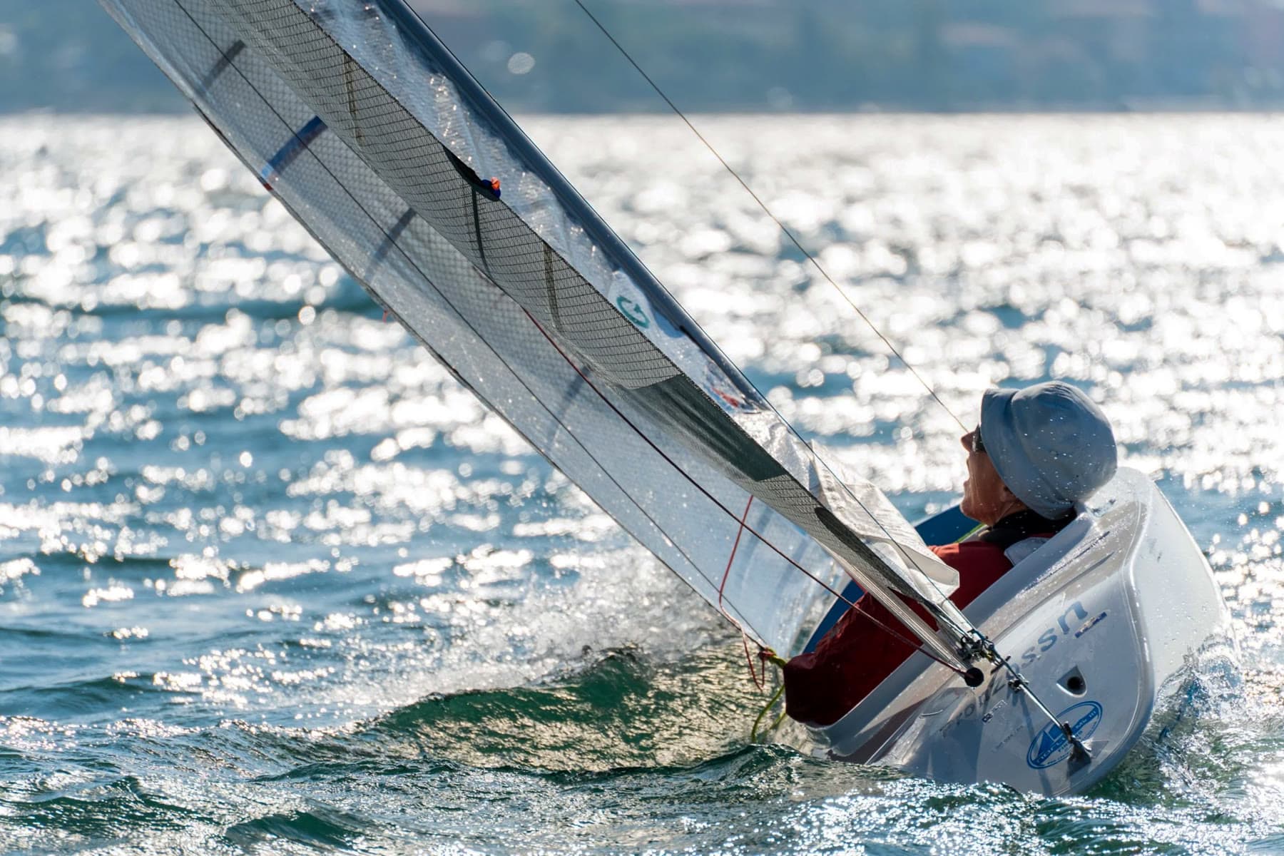 A 2.4mR heeling through a gust, backlit spray flying, the sailor hiking to windward
