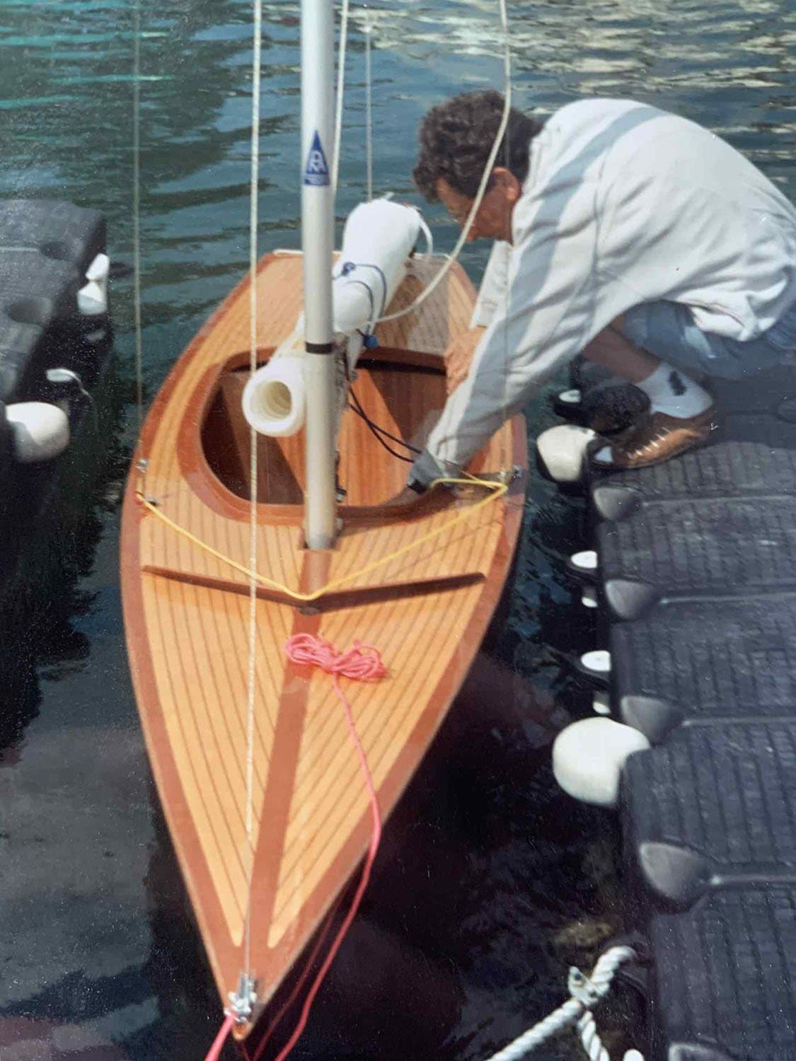 A varnished wooden Norlin 2.4mR being rigged alongside a dock.